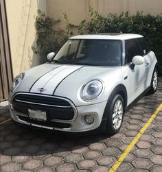 a white and black mini car parked in front of a building next to a bush