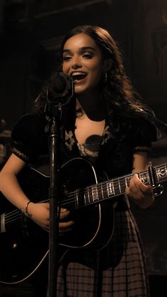 a woman singing into a microphone while holding a guitar