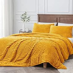 a yellow comforter set on a bed in a room with hardwood floors and white walls