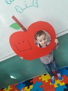 a young boy holding up a piece of puzzle with an apple shaped like a heart