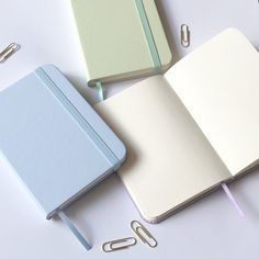 three different colored notebooks with paper clips next to them