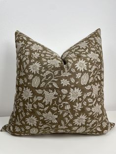 a brown and white floral pillow sitting on top of a table next to a wall