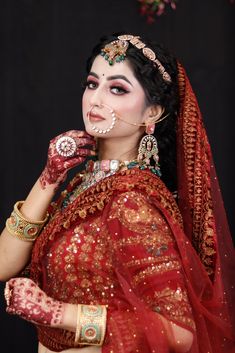 a woman in a red and gold bridal outfit with jewelry on her head, wearing an elaborate nose ring