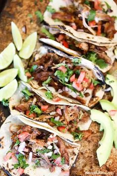 several tacos are lined up on a table with avocado slices and salsa