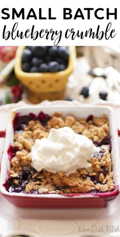 small batch blueberry crumble in a red dish with whipped cream on top and berries next to it