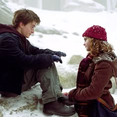 a man and woman sitting next to each other in the snow looking at their cell phones