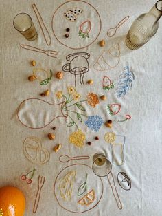 an embroidered tablecloth with various items on it, including oranges and other kitchen utensils