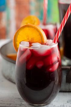 two glasses filled with red liquid and orange slices on the table next to each other