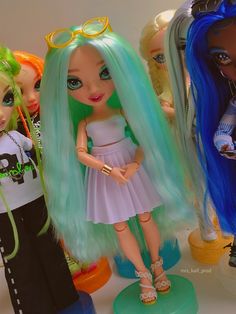 three dolls are standing next to each other in front of a white wall with blue and green hair