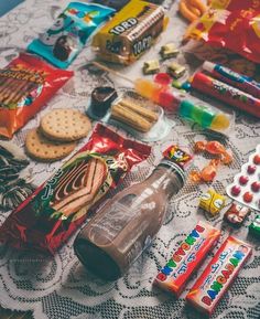 an assortment of candy, crackers, and other snacks on a tablecloth with doily