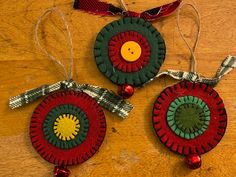 two ornaments are hanging on a wooden table with ribbons and buttons in the shape of an ornament