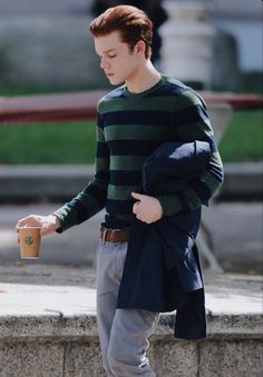 a young man walking down the street holding a cup