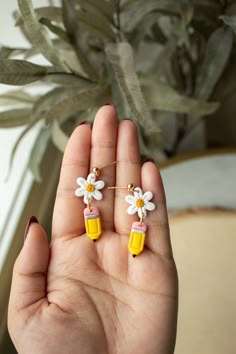 a hand holding two small yellow and white flowers on it's fingers, with a plant in the background