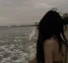 a woman standing on the back of a boat looking out at the ocean with buildings in the background