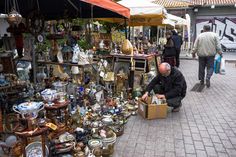 a man kneeling down in front of a display of vases and other items at an outdoor market