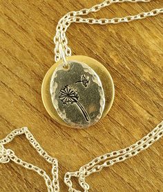 "A Minimalist Portrait of a Dandelion: A Dandelion and a fly-away seedling are hand stamped onto a silver oval with hand hammered edges. A hand polished disc of jewelers brass frames and highlights the dandelion oval of this mixed metal necklace. It hangs from an 18\" sterling silver chain but other lengths are available." Metal Stamp Jewelry, Stamp Jewelry, Minimalist Portrait, Brass Frames, Mixed Metal Necklace, The Dandelion, A Dandelion, Metal Stamped Jewelry, Jupiter Fl