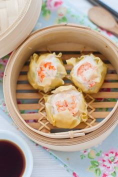 three dumplings with shrimp are in a bamboo steamer basket on a blue tablecloth