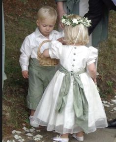 two young children dressed in white and green clothes, one holding a basket while the other is