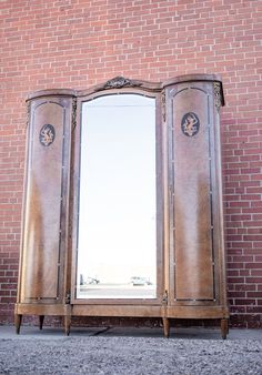 an old wooden armoire sitting in front of a brick wall with two mirrors on it