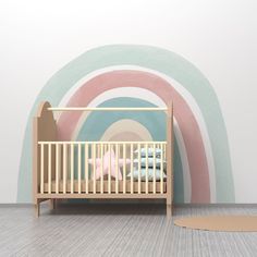 a baby's bed in front of a wall with a rainbow painted on it