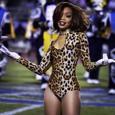 a woman in leopard print bodysuit and white gloves on the sidelines at a football game