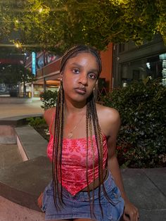 a woman with long braids is sitting on the curb and looking at the camera