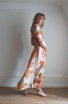 a woman in a long dress is standing against a wall