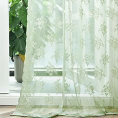 a green curtain with white flowers on it next to a potted plant in front of a window