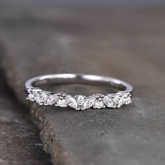 a white gold wedding band with five diamonds on the top and bottom, sitting on a rock