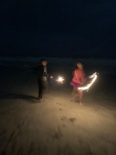 two people standing in the sand holding sparklers