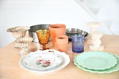 a table topped with plates and vases on top of a wooden table