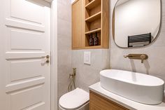 a white toilet sitting under a bathroom mirror next to a sink and wooden cabinetry