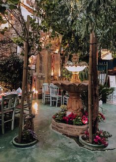 an outdoor dining area with tables, chairs and a fountain in the center surrounded by trees