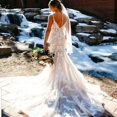 a woman standing in front of a waterfall wearing a wedding dress with an open back