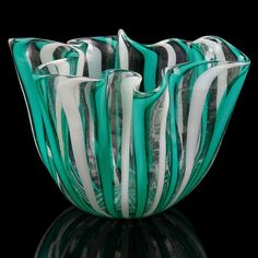 a green and white glass bowl sitting on top of a black table next to a mirror