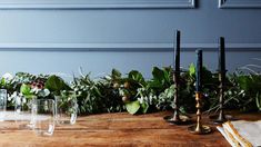 a wooden table topped with lots of greenery next to glasses and candlesticks