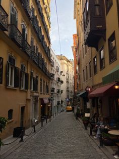 an empty cobblestone street with people sitting at tables in the distance and buildings on either side