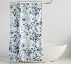 a blue and white floral shower curtain next to a bathtub with a sink in the background