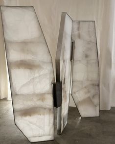 two white marble sculptures sitting on top of a cement floor in front of a curtain