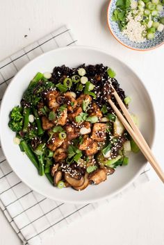 a white bowl filled with chicken, broccoli and sesame seed salad next to chopsticks