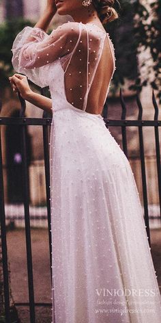 a woman in a white dress leaning on a fence with her back to the camera