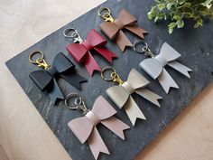 six leather bow keychains sitting on top of a black slate board next to a potted plant