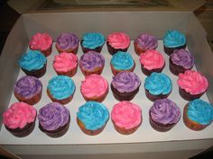 there are many cupcakes in the box with frosting on them and pink, blue, and purple icing