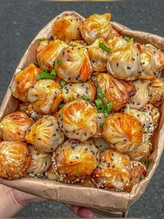 a person holding up a box filled with dumplings covered in sesame seeds and vegetables