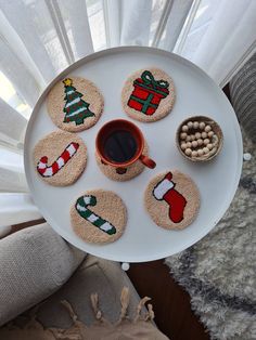 a white plate topped with coasters covered in christmas themed decorations next to a cup of coffee