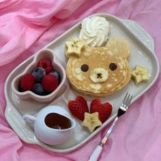 a white plate topped with pancakes and fruit next to a cup of coffee on top of a pink blanket