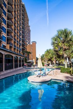 an outdoor swimming pool with lounge chairs and umbrellas next to the resort's large building