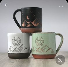 three coffee mugs sitting next to each other on top of a wooden table in front of a white wall