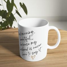 a white coffee mug sitting on top of a wooden table next to a potted plant