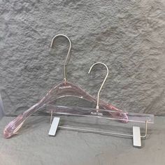 a pair of clear plastic hangers on a gray background with white tags attached to them